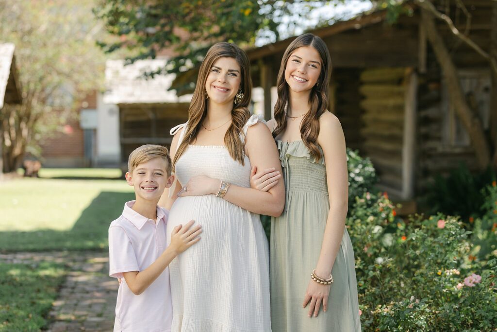 Mom in cream dress standing outdoors with daughter and son during a fall maternity session in Shreveport, Louisiana.