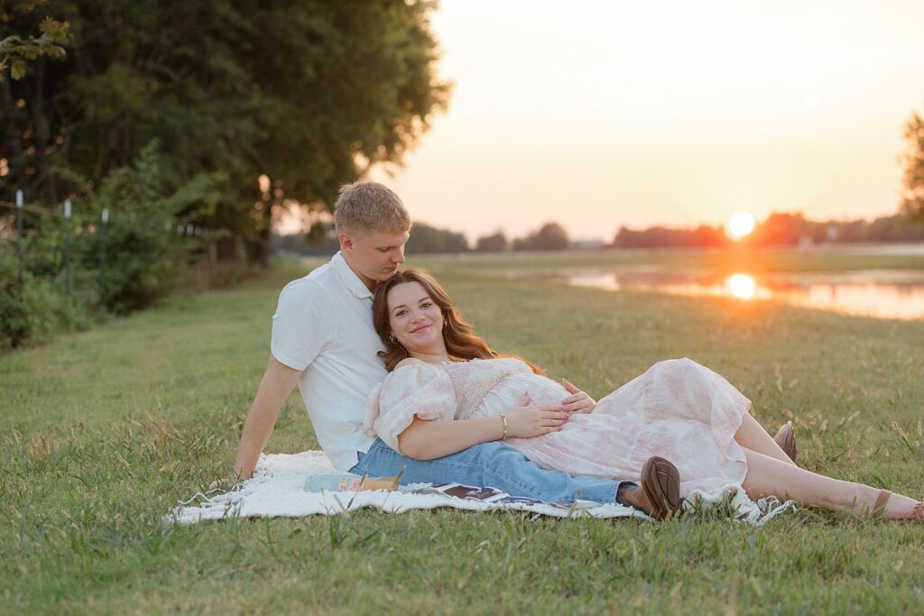 Couple posing for maternity pictures in front of the sunset.