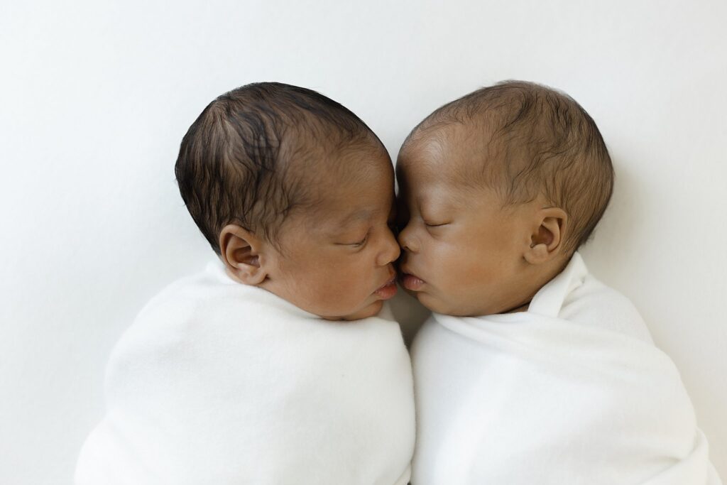 Twins cuddling face to face on white backdrop