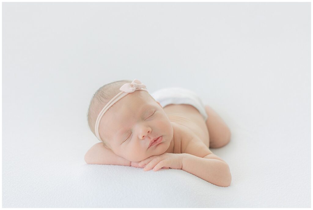 Sleeping newborn baby girl with bow headband posed on white blanket in Shreveport studio – newborn detail photography Shreveport