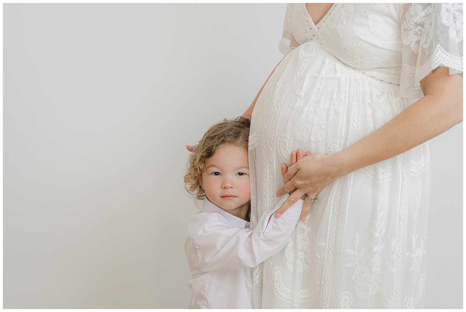 studio maternity photos with toddler sibling touching pregnant mom’s belly during Shreveport maternity session